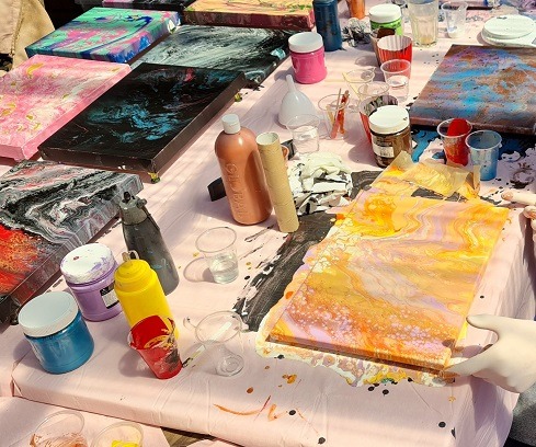 A woman is engaging in paint pouring on a table with colorful paints for an art therapy experience. Abstract Art by Thanh Lyons