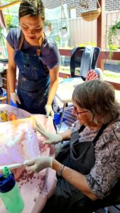 A woman is working on a paint pouring project with an older woman who has years of experience. Abstract Art by Thanh Lyons