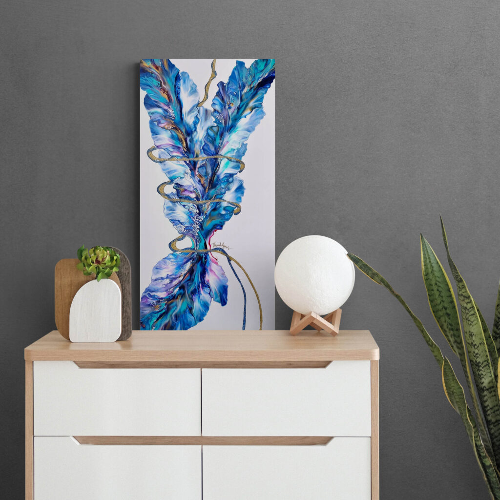 A blue and white Cosmic Dance painting on a dresser next to a potted plant. Abstract Art by Thanh Lyons