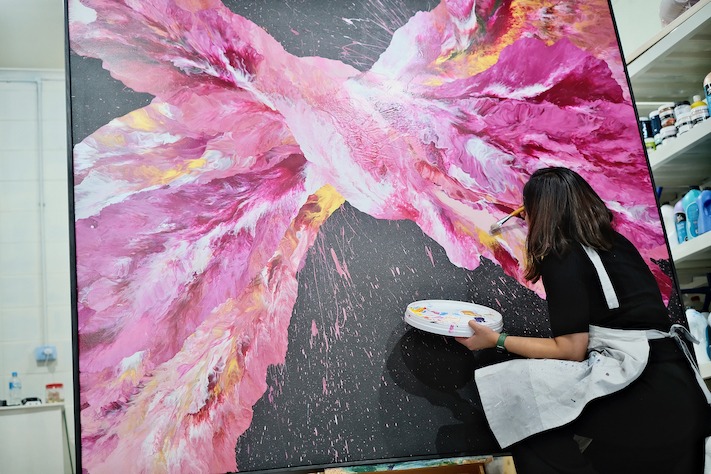 A woman painting a large pink art commission in a studio. Abstract Art by Thanh Lyons