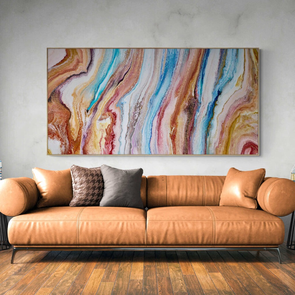 A colorful abstract painting called Chasing Sands (92 x 183 cm - Framed) hangs above a leather couch in a living room. Abstract Art by Thanh Lyons